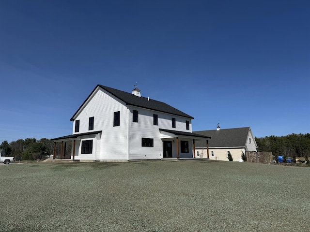 back of house with a chimney and a shingled roof