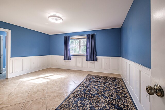 spare room featuring a wainscoted wall, a decorative wall, and tile patterned floors