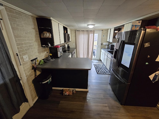kitchen featuring black fridge, dark wood-style floors, stainless steel range with electric cooktop, brick wall, and a peninsula