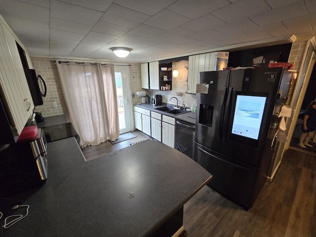 kitchen featuring open shelves, black fridge, a sink, brick wall, and dishwasher