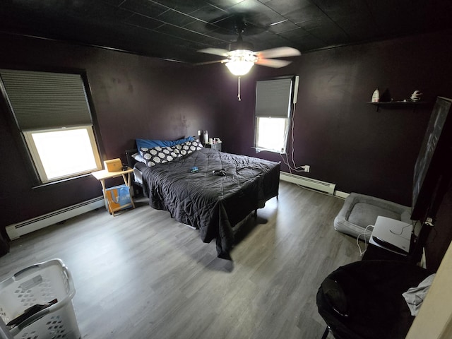 bedroom with multiple windows, baseboard heating, and wood finished floors