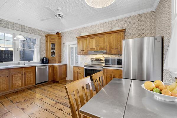 kitchen featuring brown cabinetry, appliances with stainless steel finishes, under cabinet range hood, wallpapered walls, and light wood-style flooring