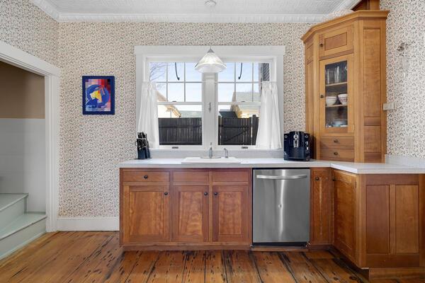 bar with stainless steel dishwasher, a sink, light wood finished floors, and wallpapered walls