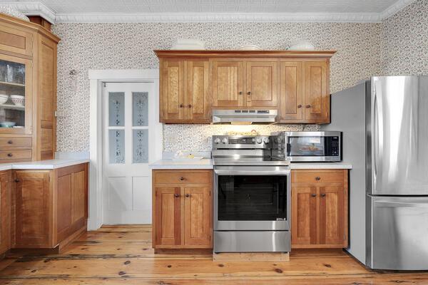kitchen featuring light countertops, light wood-style flooring, stainless steel appliances, wallpapered walls, and under cabinet range hood