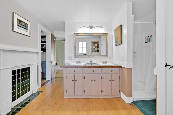 full bath with a sink, double vanity, baseboards, wood finished floors, and a stall shower