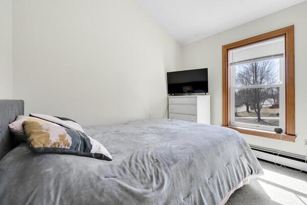 carpeted bedroom featuring vaulted ceiling and a baseboard heating unit