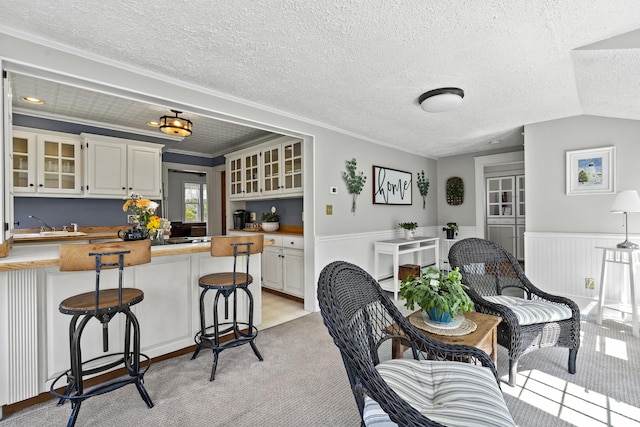 294 E Pond Rd, Jefferson, ME 04348 - kitchen featuring a breakfast bar area, glass insert cabinets, butcher block countertops, a wainscoted wall, and light carpet