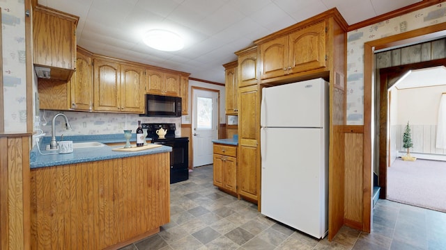kitchen with a sink, crown molding, black appliances, wainscoting, and wallpapered walls