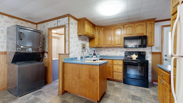 kitchen with wallpapered walls, stacked washer and clothes dryer, wainscoting, and black appliances