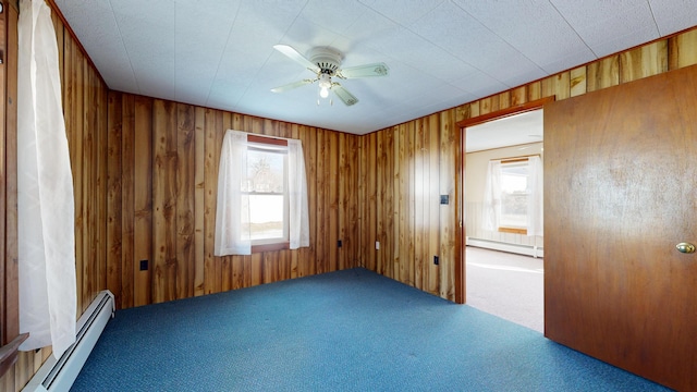 carpeted spare room with wood walls, a baseboard radiator, and a ceiling fan