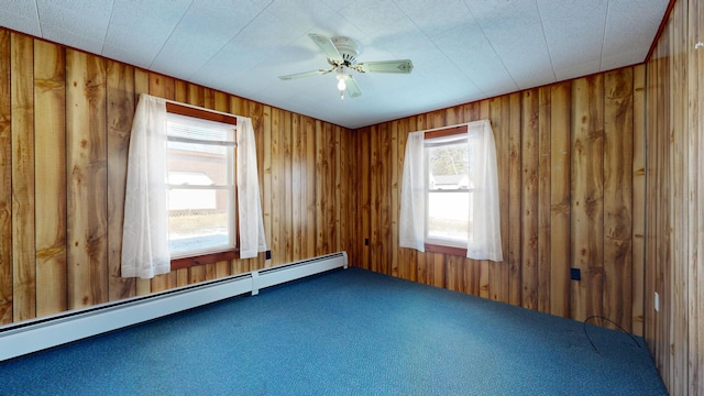 carpeted spare room with wooden walls, a baseboard radiator, and ceiling fan
