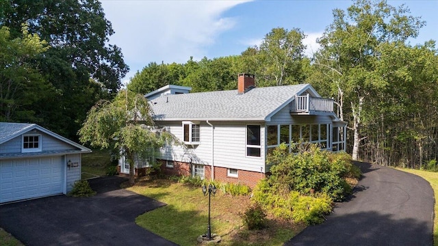 view of side of home with aphalt driveway, a detached garage, an outdoor structure, roof with shingles, and a chimney