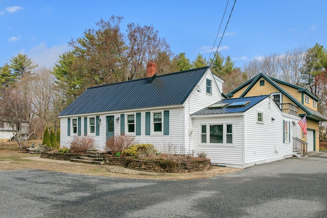view of front facade featuring a garage, driveway, a chimney, and metal roof