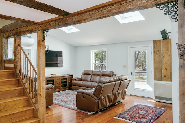 living room featuring vaulted ceiling with skylight, stairway, a wall unit AC, and wood finished floors