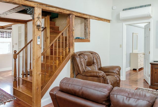 living room featuring wood finished floors, beam ceiling, baseboards, a wall mounted AC, and stairs