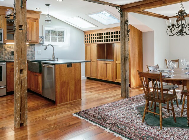 kitchen featuring stainless steel dishwasher, light wood-style flooring, a sink, dark countertops, and decorative backsplash