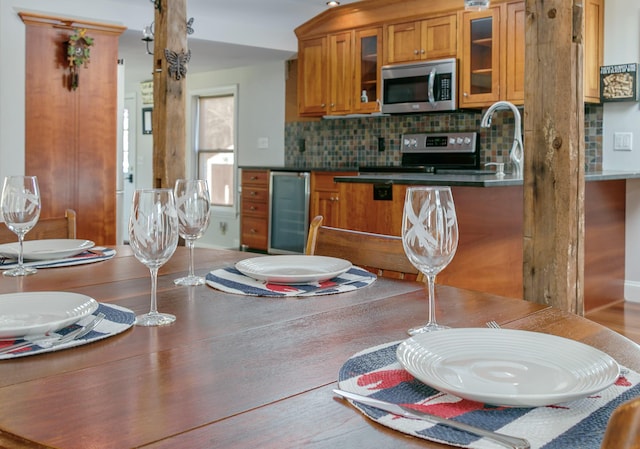 kitchen featuring brown cabinets, decorative backsplash, beverage cooler, glass insert cabinets, and stainless steel appliances