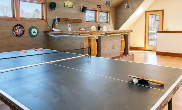 recreation room featuring light wood finished floors, vaulted ceiling, baseboards, and bar
