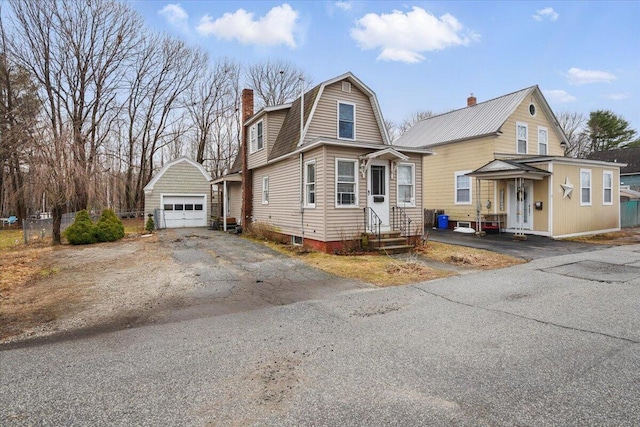 view of front of home featuring a chimney, a detached garage, entry steps, an outbuilding, and a gambrel roof