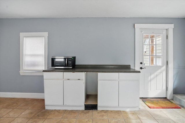 interior space featuring white cabinetry, light tile patterned flooring, stainless steel microwave, dark countertops, and baseboards