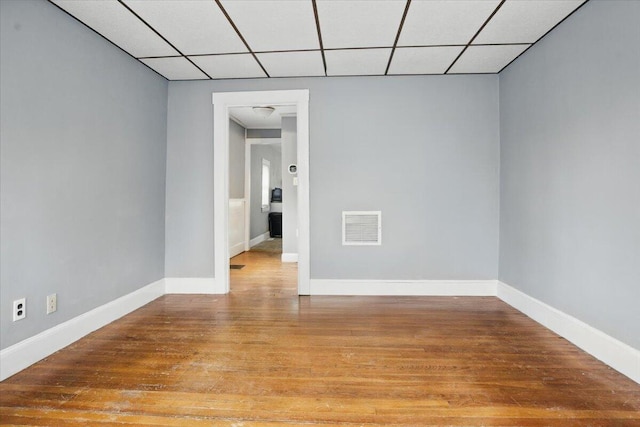 unfurnished room featuring visible vents, light wood-style flooring, a drop ceiling, and baseboards