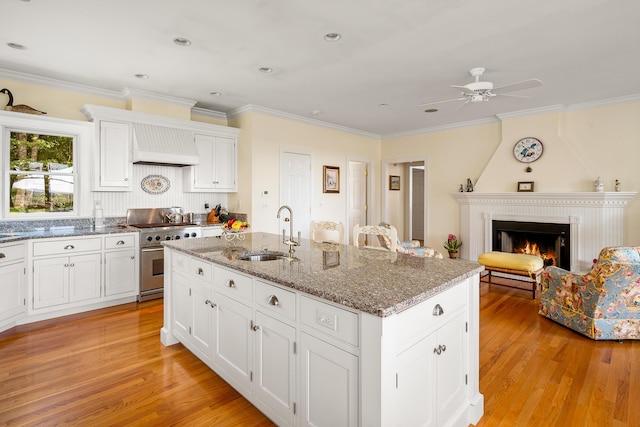 21 Bristol Dr, Rockport, ME 04856 - kitchen featuring stainless steel stove, a lit fireplace, premium range hood, a ceiling fan, and a sink