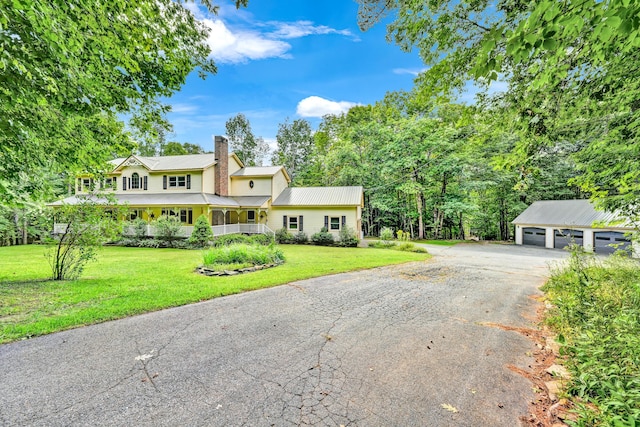 view of front of house featuring a front yard, a garage, aphalt driveway, a chimney, and an outdoor structure