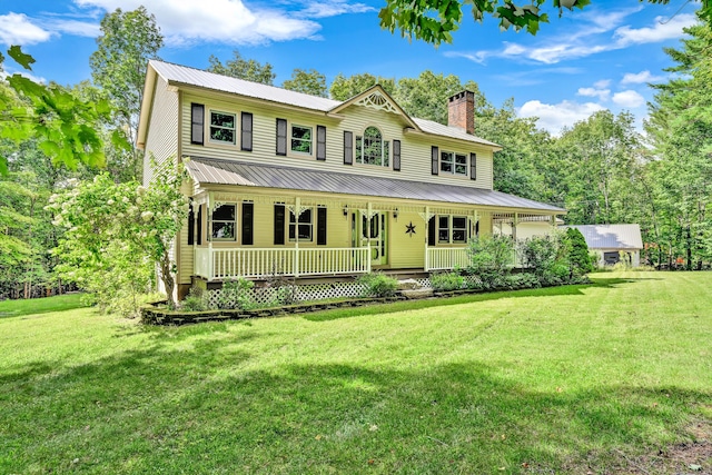 view of front of home featuring a chimney, covered porch, a front yard, and metal roof