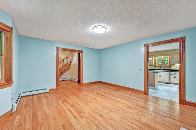 empty room featuring stairway, light wood-style flooring, a baseboard heating unit, and a sink