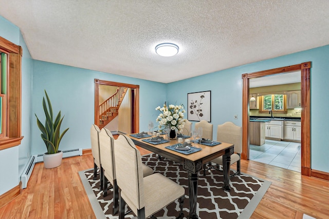 dining space with a baseboard radiator, a textured ceiling, stairway, and light wood-style floors