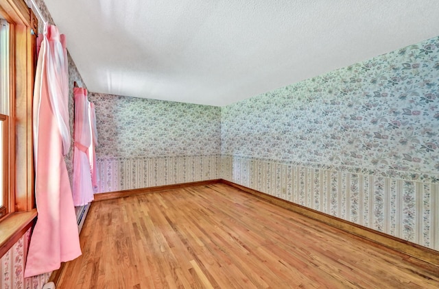 unfurnished room with baseboards, light wood finished floors, a textured ceiling, and wallpapered walls