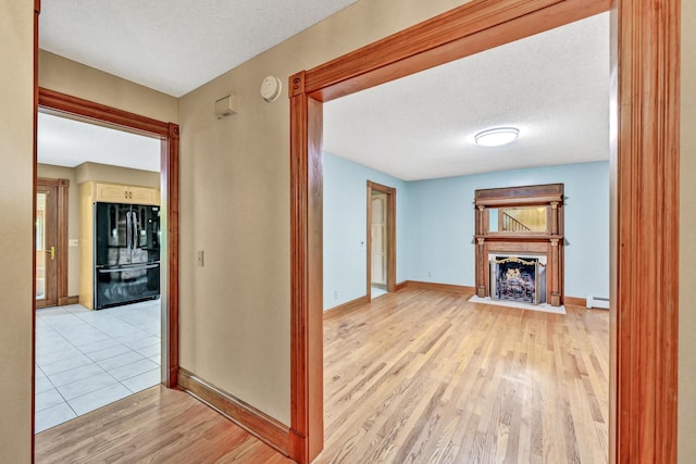 corridor with baseboards, light wood-type flooring, a baseboard heating unit, and a textured ceiling