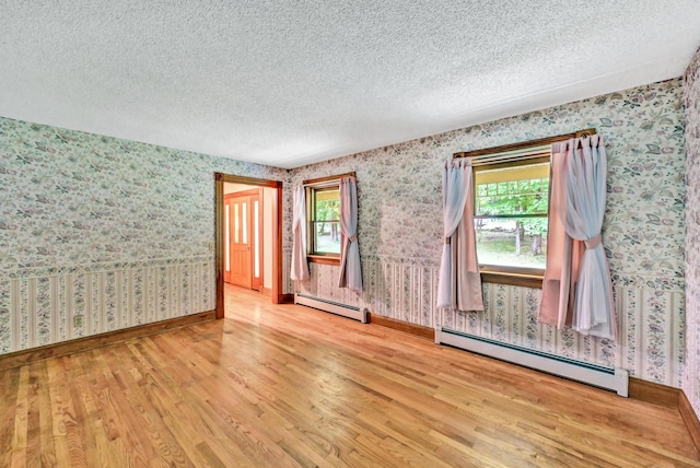 spare room featuring a wealth of natural light, a baseboard heating unit, wood finished floors, and wallpapered walls