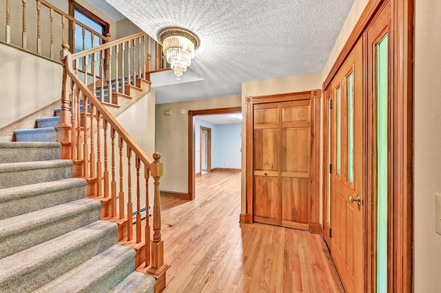 staircase with baseboards, a chandelier, a textured ceiling, a baseboard radiator, and wood finished floors