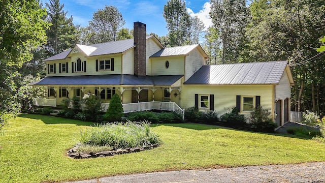 view of front facade with a porch, a chimney, metal roof, and a front lawn
