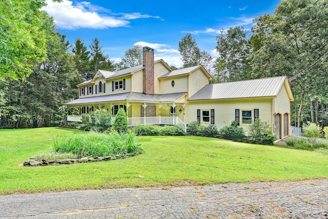 view of front of property featuring a front yard, metal roof, covered porch, and a chimney