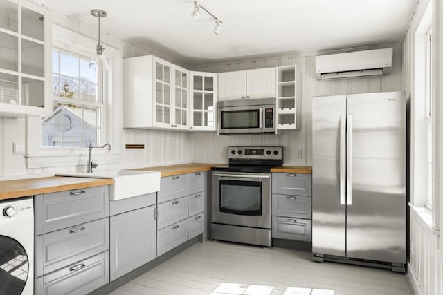 9 School St, Boothbay Harbor, ME 04538 - kitchen with washer / clothes dryer, an AC wall unit, wood counters, gray cabinetry, and appliances with stainless steel finishes