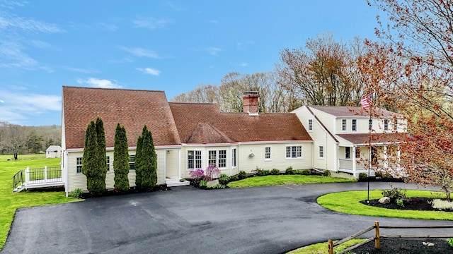 view of front of property featuring aphalt driveway, a chimney, and a front yard