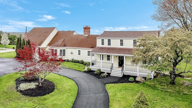 view of front of home with covered porch, roof with shingles, a chimney, and a front yard