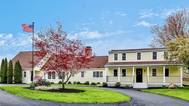 view of front of house featuring covered porch, a chimney, and a front lawn