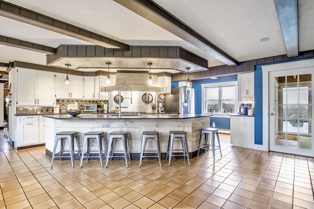 kitchen featuring stainless steel fridge, dark countertops, beamed ceiling, decorative backsplash, and light tile patterned flooring
