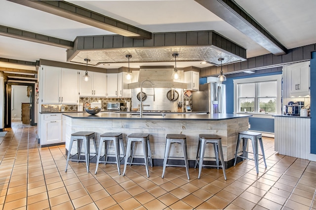 kitchen featuring beam ceiling, decorative backsplash, light tile patterned floors, stainless steel fridge with ice dispenser, and dark countertops