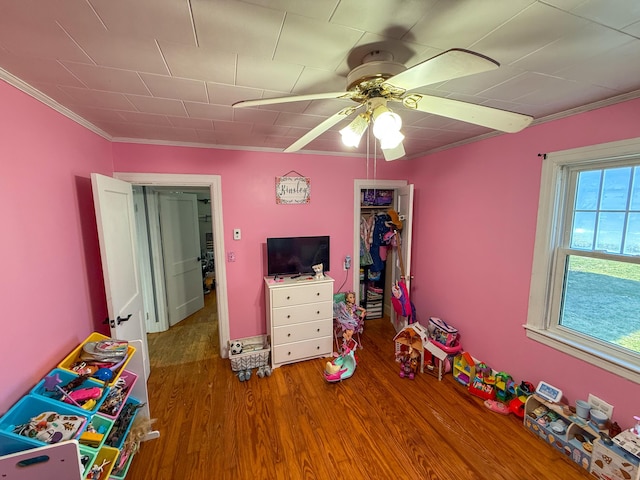rec room with wood finished floors, ceiling fan, and ornamental molding