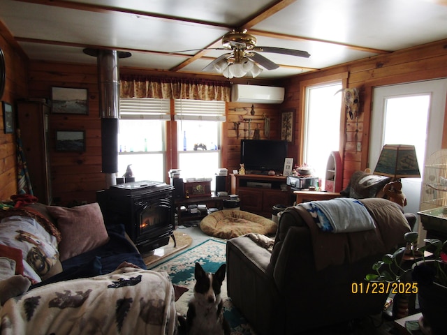 living room featuring wood walls, a wood stove, ceiling fan, and plenty of natural light