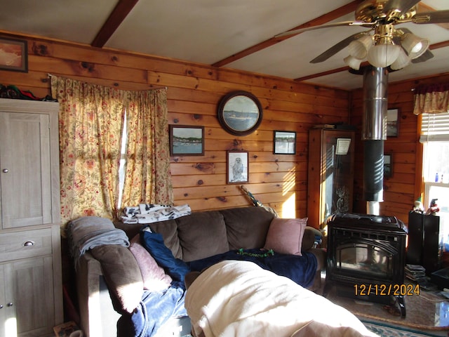 living room featuring wooden walls, beam ceiling, a wood stove, and a ceiling fan