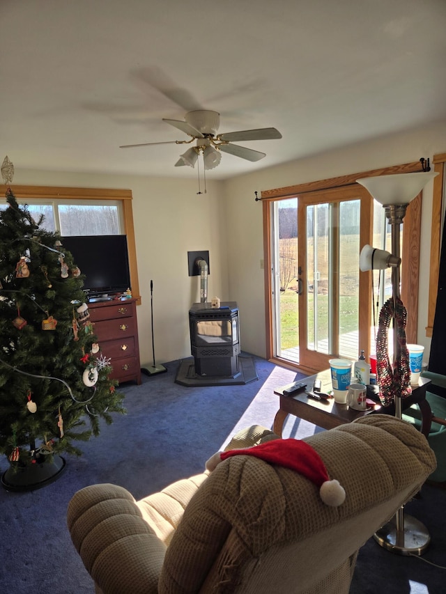 living room featuring a wood stove, ceiling fan, and carpet