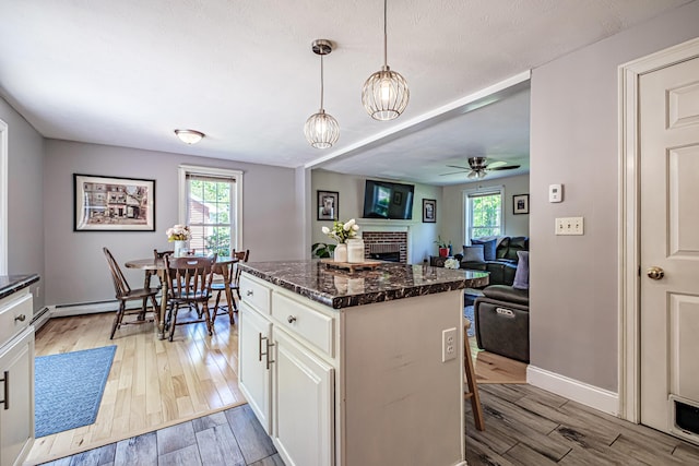 18 Sheila Cir, Saco, ME 04072 - kitchen featuring light wood-style flooring, a fireplace, a ceiling fan, dark stone counters, and white cabinetry