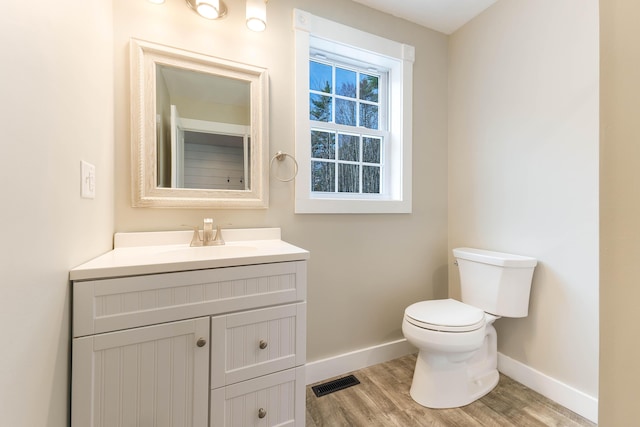 half bathroom with visible vents, baseboards, toilet, wood finished floors, and vanity