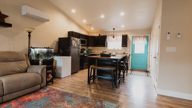 kitchen with open floor plan, an AC wall unit, light wood-type flooring, stainless steel microwave, and vaulted ceiling