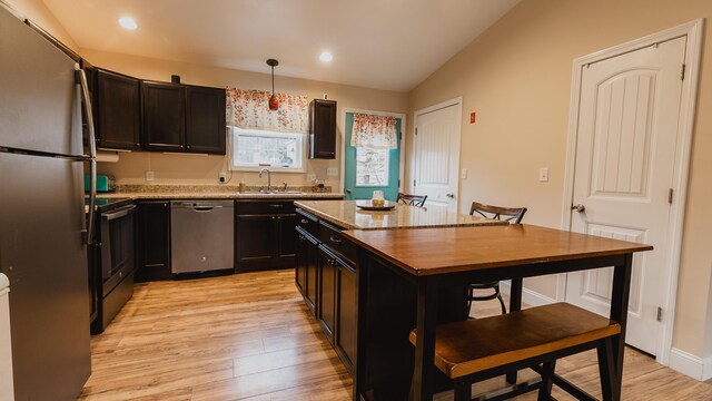 kitchen featuring light wood-type flooring, appliances with stainless steel finishes, a sink, and vaulted ceiling